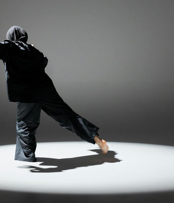 Woman performing a light cardio movement in a dark studio with golden light.